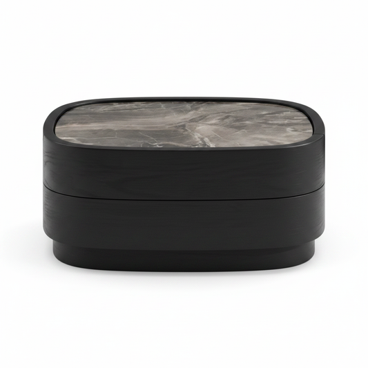 Low rounded matte black bedside table with dark grey veined marble top and handleless drawer, front view on white background