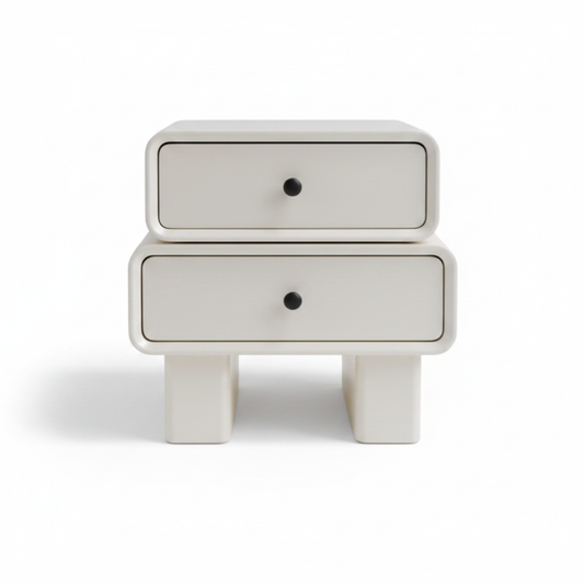 Warm cream matte two-drawer bedside table with black knob handles on chunky architectural legs, front view on white background